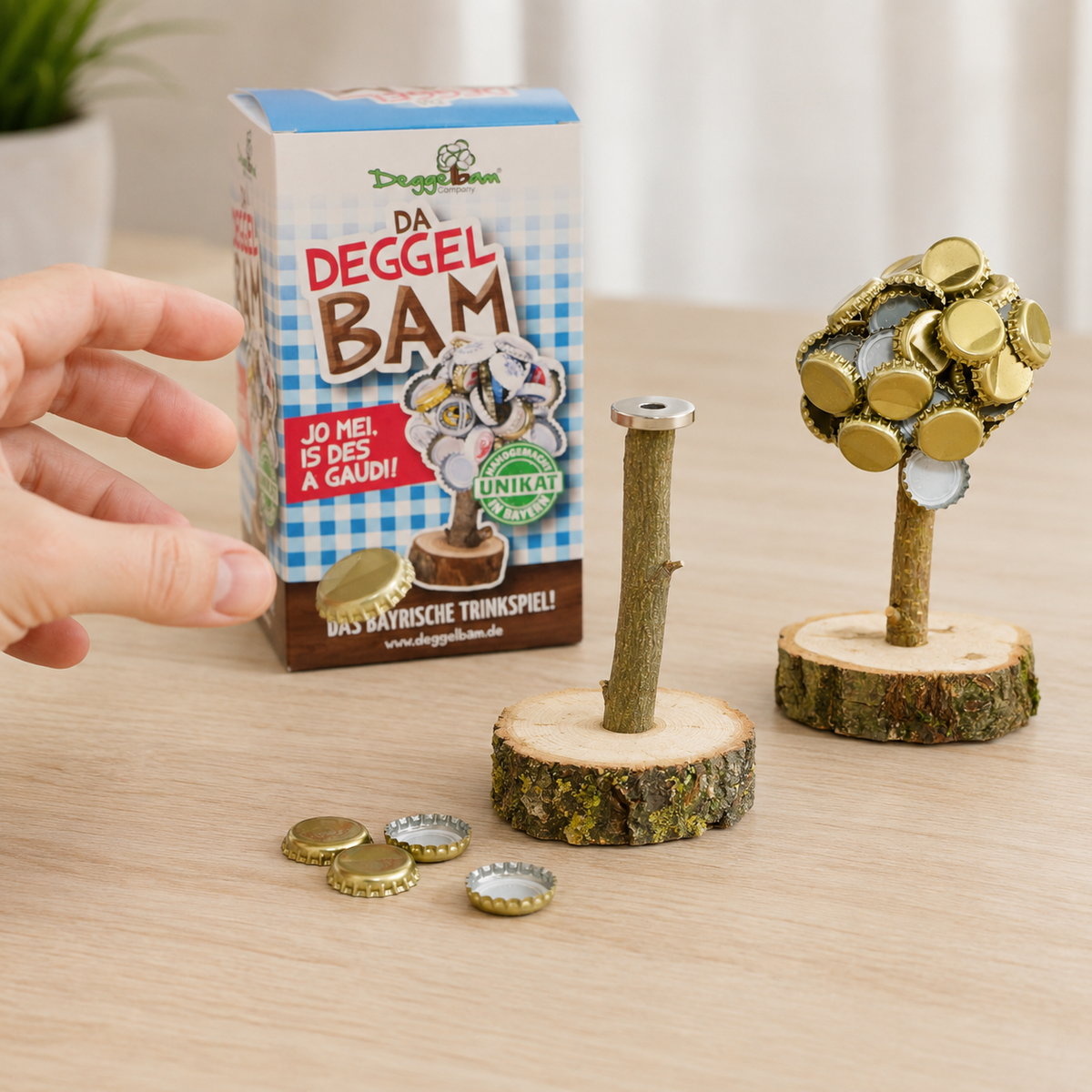 Zwei Deggelbäume mit und ohne Kronkorken neben der Verpackung; eine Hand nähert sich dem Magneten.